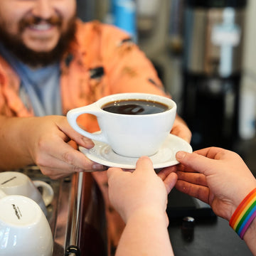 Person receiving a cup of coffee from another person in a coffee shop setting.