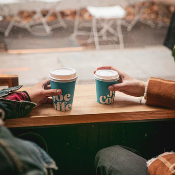 Two people holding coffee cups with 'Joe Coffee' branding at a cafe.