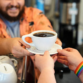 Person receiving a cup of coffee from another person in a coffee shop setting.