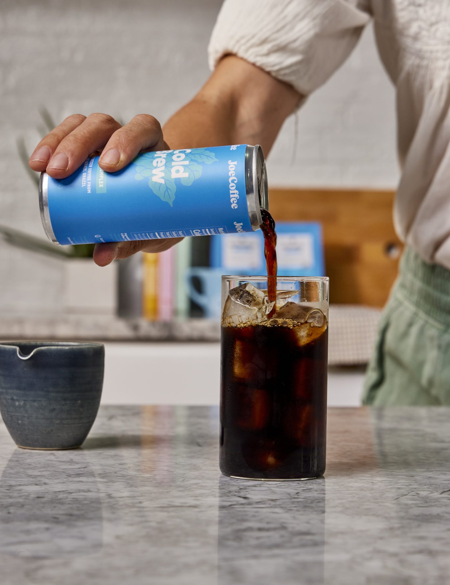 Person pouring a cold brew can into a glass with ice