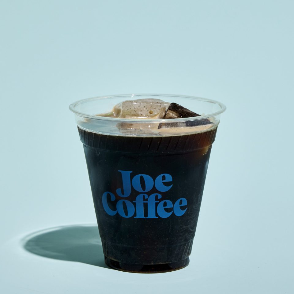 Clear compostable cup of cold brew on a light blue background