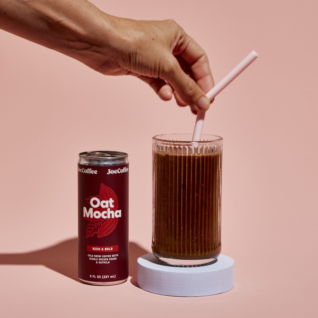 Oat mocha can and cup side by side with a hand inserting a straw into the cup