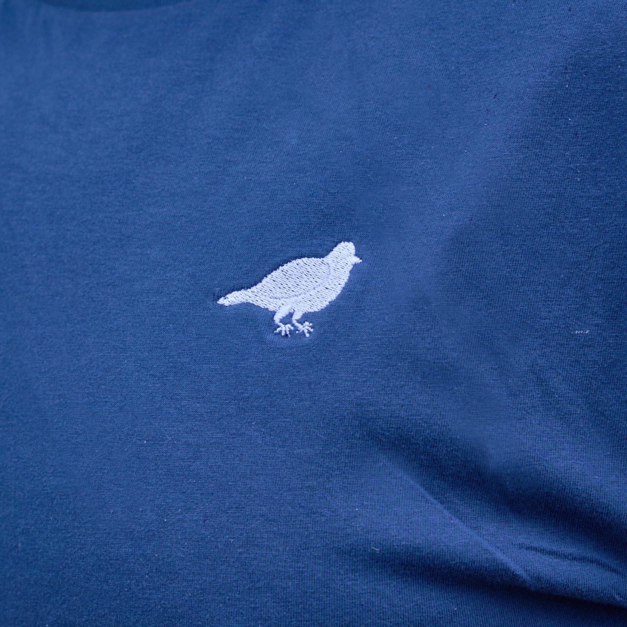 Detail shot of navy blue shirt front side with pigeon embroidered on left side